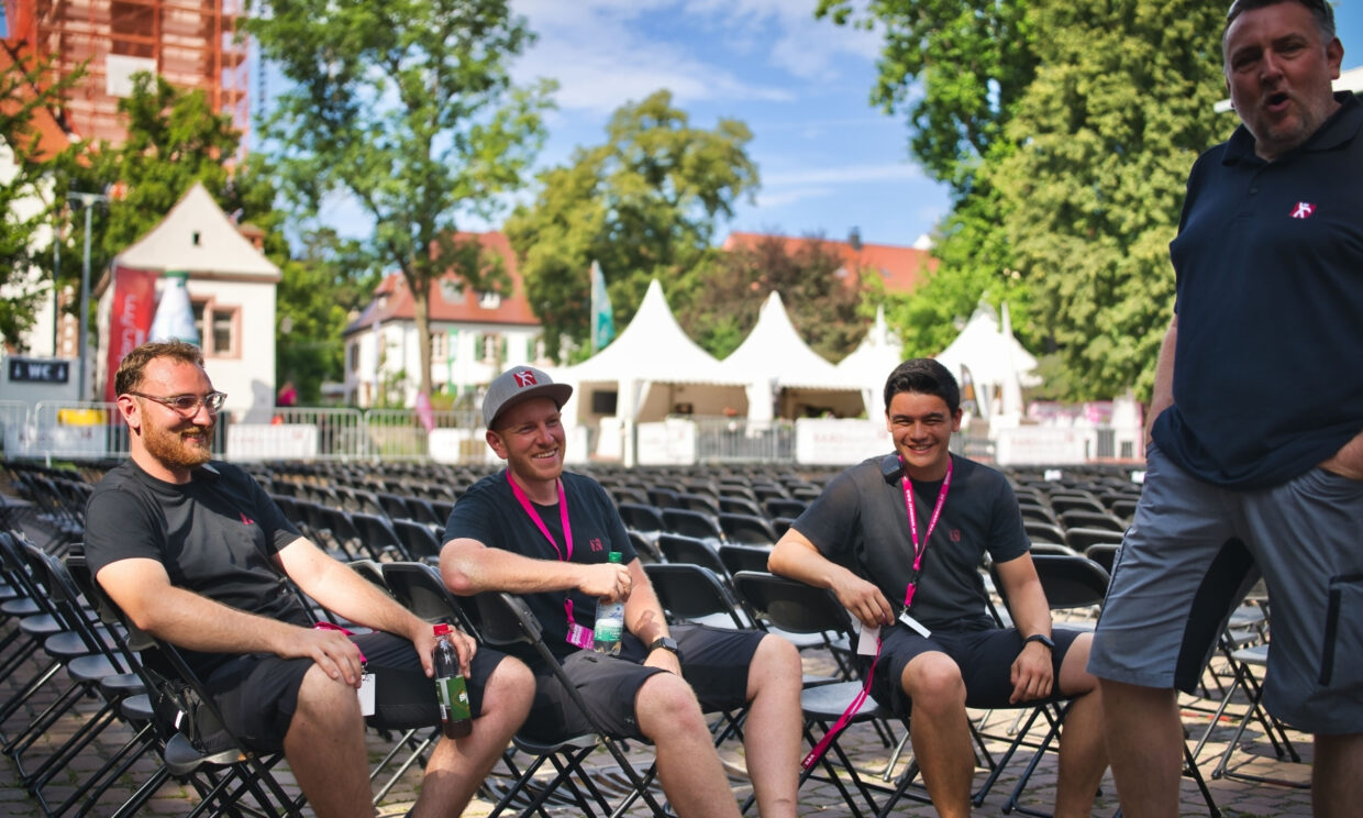 3 Männer sitzen auf Stühlen einer steht alle lachen